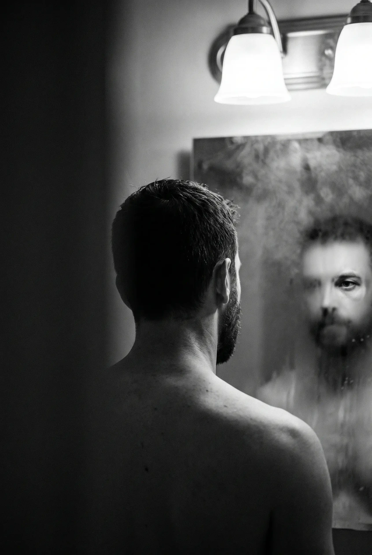 Hombre frente al espejo en un baño, retrato editorial en blanco y negro